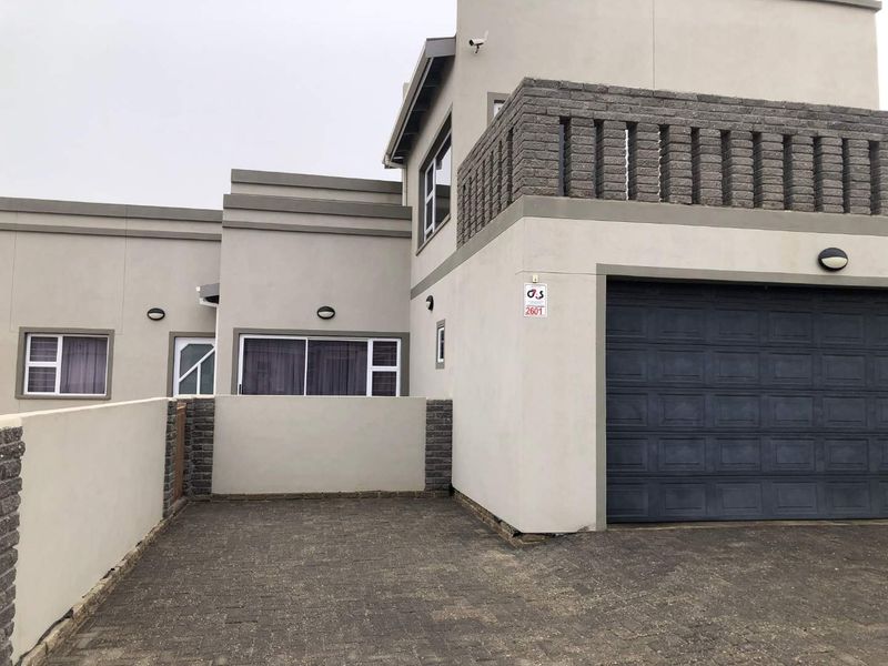 Front elevation of a modern house featuring a paved driveway, integrated garage, and an upper-level balcony with a decorative masonry balustrade.