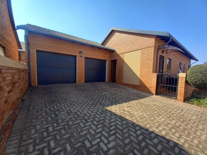 Front view of a townhouse featuring a double garage, paved driveway, and brick exterior facade with a secure entrance gate.