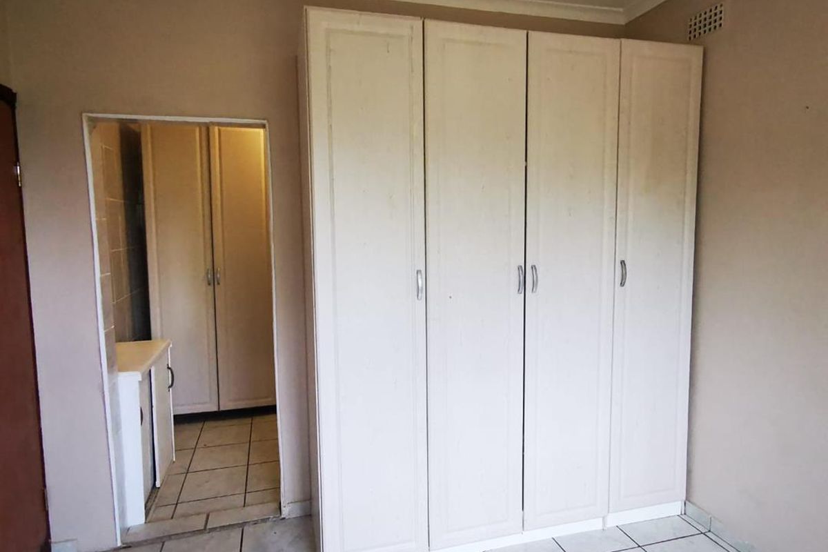 A bedroom featuring built-in wardrobes, tiled flooring, and an adjoining space, likely a bathroom or dressing area.