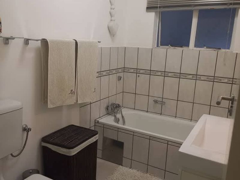 A functional bathroom featuring a bathtub with tiled surround, a vanity basin, and a toilet, finished with neutral wall and floor tiles.