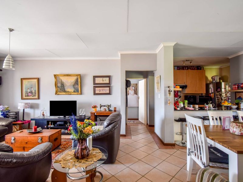 Open-plan living and dining area featuring tiled flooring, a breakfast bar, and an adjoining kitchen with wooden cabinetry.
