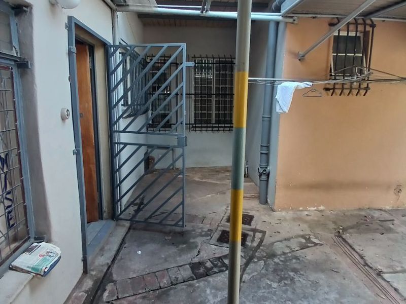 A rear exterior courtyard area featuring concrete paving, security gates, and protective window bars, providing a functional outdoor space for the apartment.