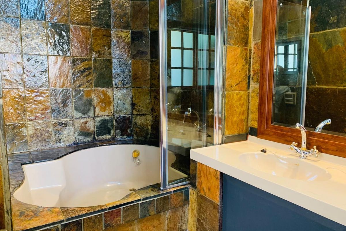 Bathroom featuring a built-in corner bathtub, glass shower enclosure, and a vanity with a basin, finished with rustic slate-style wall and floor tiling.