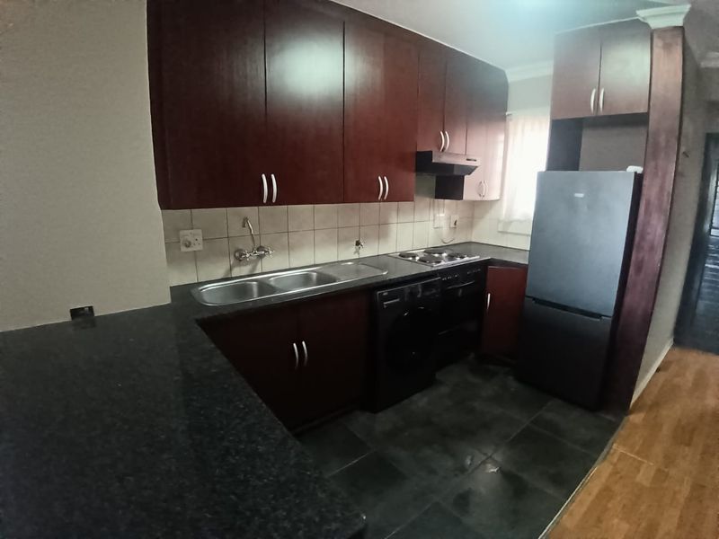 A functional kitchen featuring dark wood cabinetry, granite countertops, a double bowl sink, and built-in cooking appliances with a tiled backsplash.