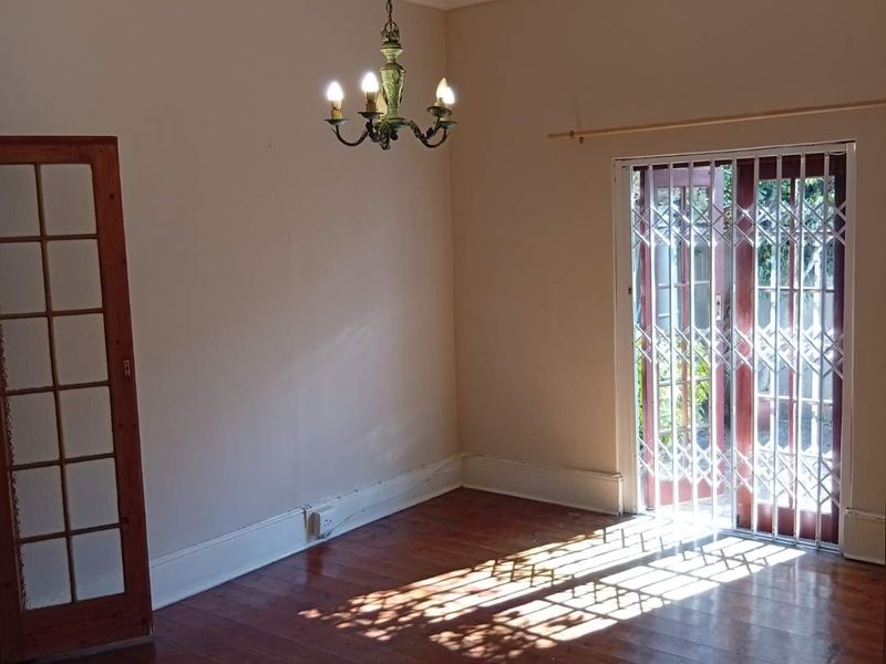 An empty living room featuring polished timber flooring, a classic chandelier, and a secure glass door leading to the exterior.