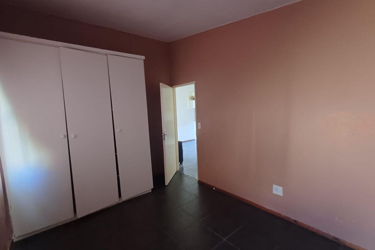 A simple, empty bedroom featuring dark tiled flooring and a white built-in wardrobe, offering a clean canvas for personalization.