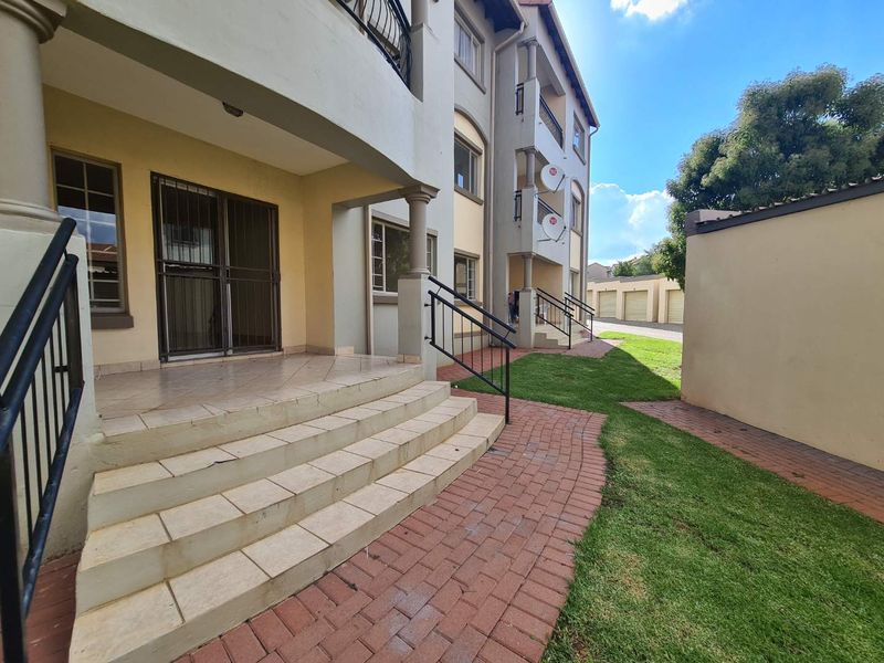 Exterior view of an apartment complex featuring a tiled patio, brick paved walkways, landscaped lawn, and secure metal railings.