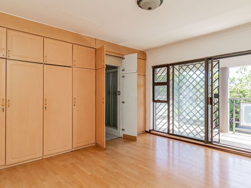 Spacious bedroom featuring extensive built-in wooden cupboards, laminate flooring, and a sliding door providing access to an outdoor balcony area.