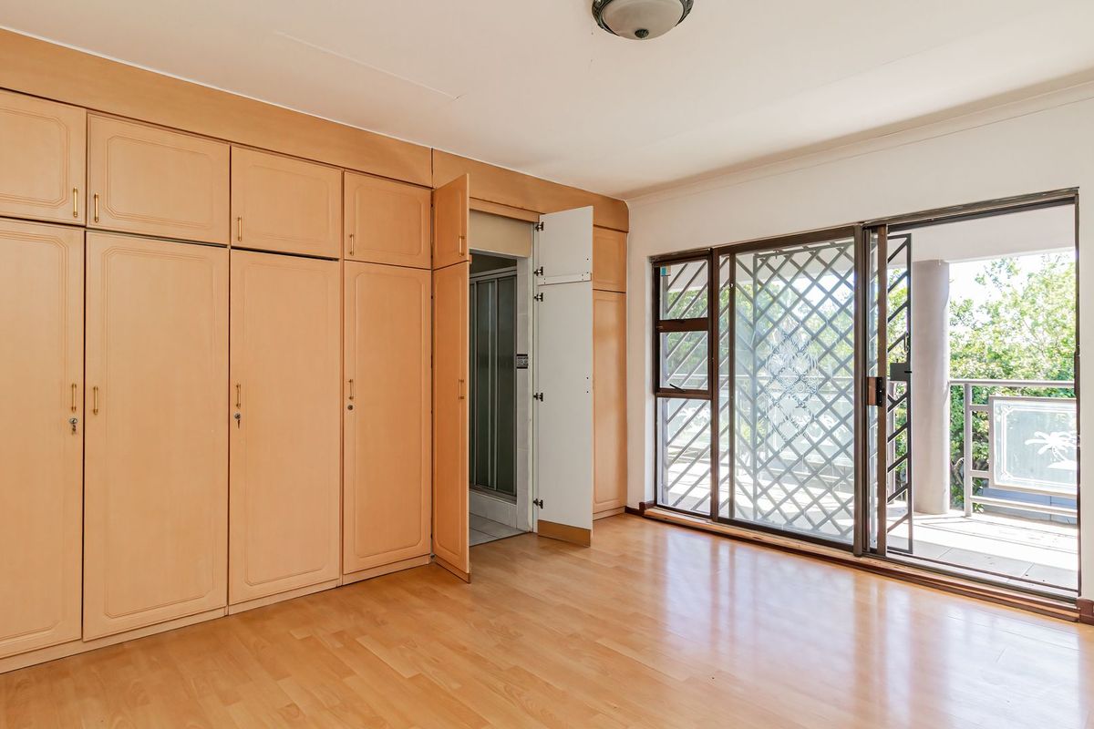 Spacious bedroom featuring extensive built-in wooden cupboards, laminate flooring, and a sliding door providing access to an outdoor balcony area.