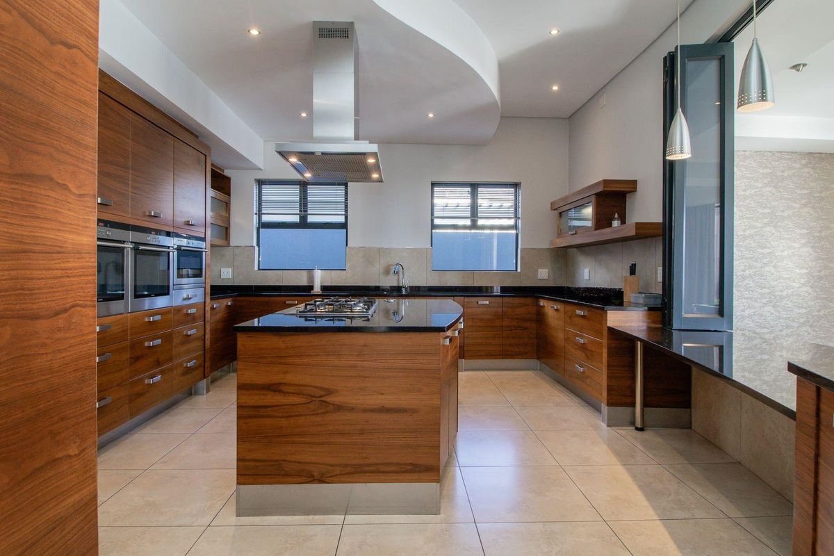 Modern kitchen featuring high-end wood cabinetry, granite countertops, a central island with a gas hob, and integrated stainless steel appliances.