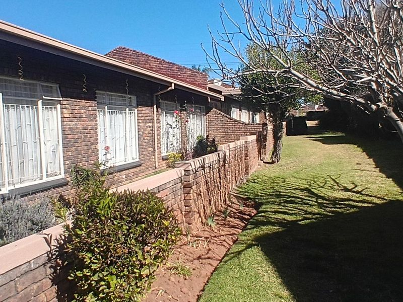A view of the rear exterior of the townhouse, featuring a face-brick facade, tiled roof, and a private garden area with a brick retaining wall.