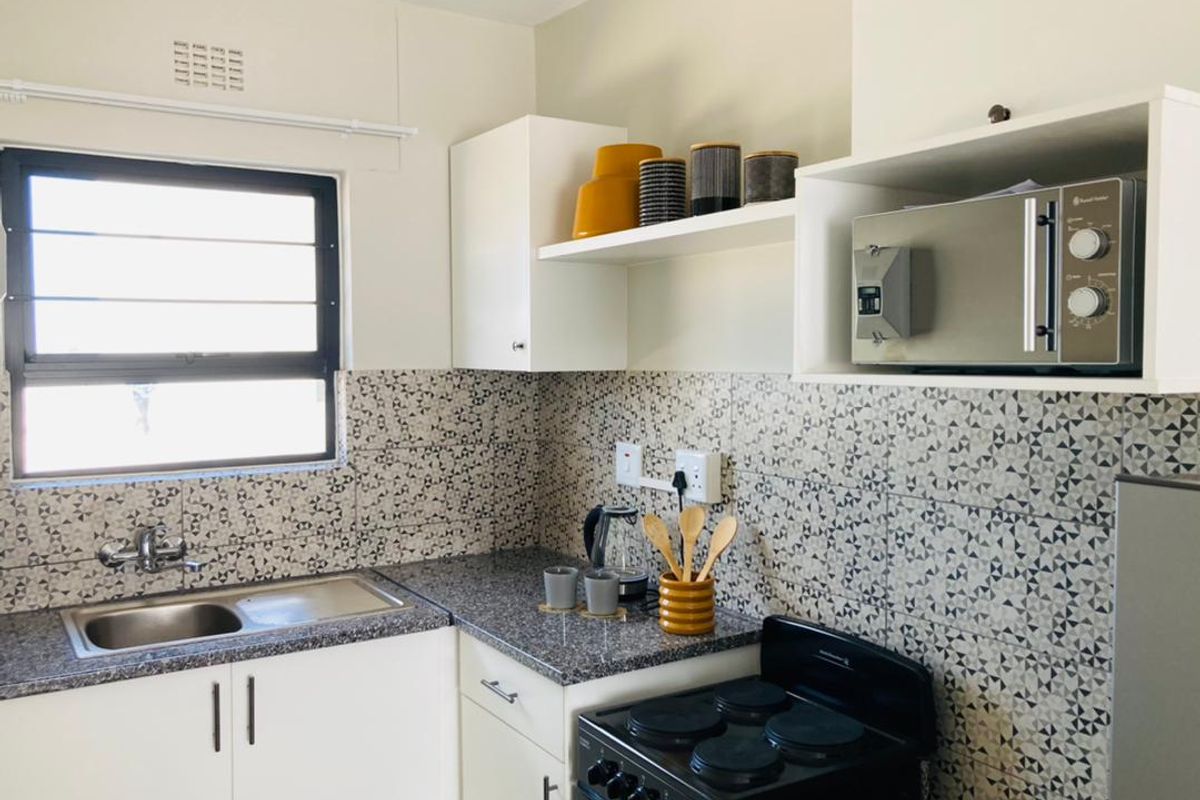A functional kitchen featuring white cabinetry, granite countertops, a geometric tiled backsplash, and a built-in microwave shelf.
