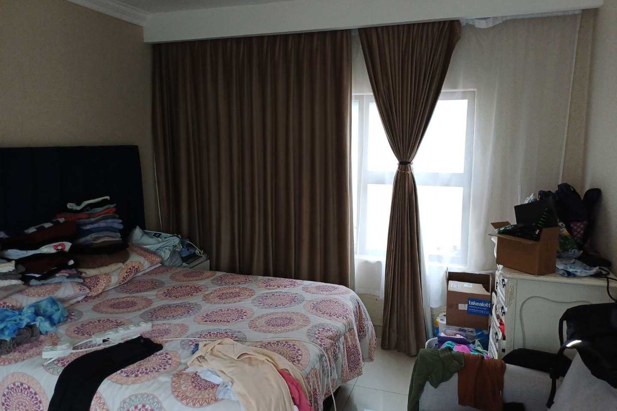 A bedroom featuring tiled flooring and full-length window curtains.