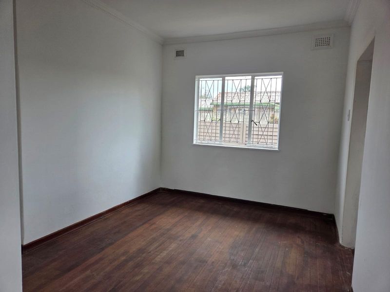 An empty bedroom featuring original wooden flooring, white walls, and a window fitted with security bars.
