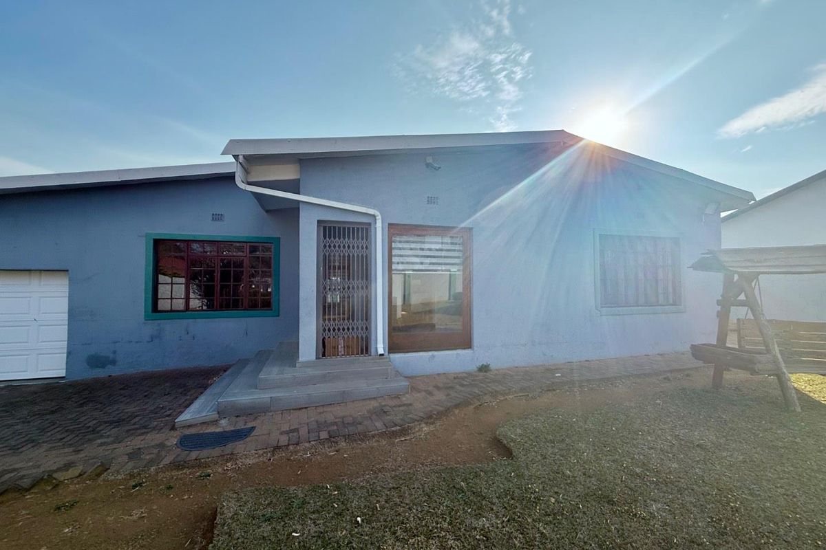 Rear view of the house featuring a paved patio area, security gate entrance, and access to the garage.