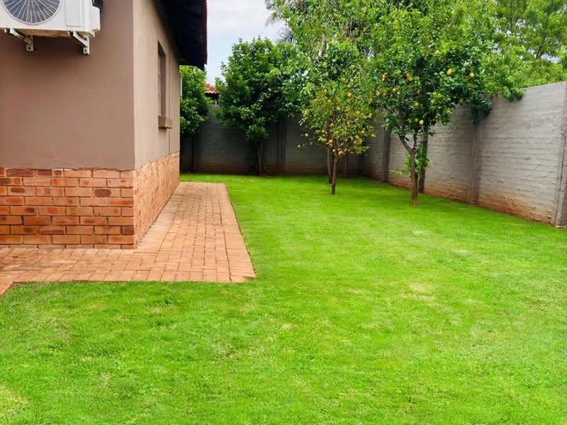 A well-maintained rear garden featuring a lush lawn, mature fruit trees, a paved walkway, and a secure boundary wall.