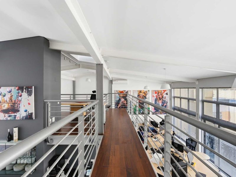 Modern open-plan office mezzanine featuring timber flooring, exposed structural steel beams, and a sleek metal balustrade overlooking the main workspace.