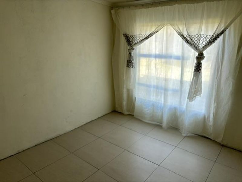 An empty bedroom featuring tiled flooring and a large window, providing a blank canvas for potential interior design updates.