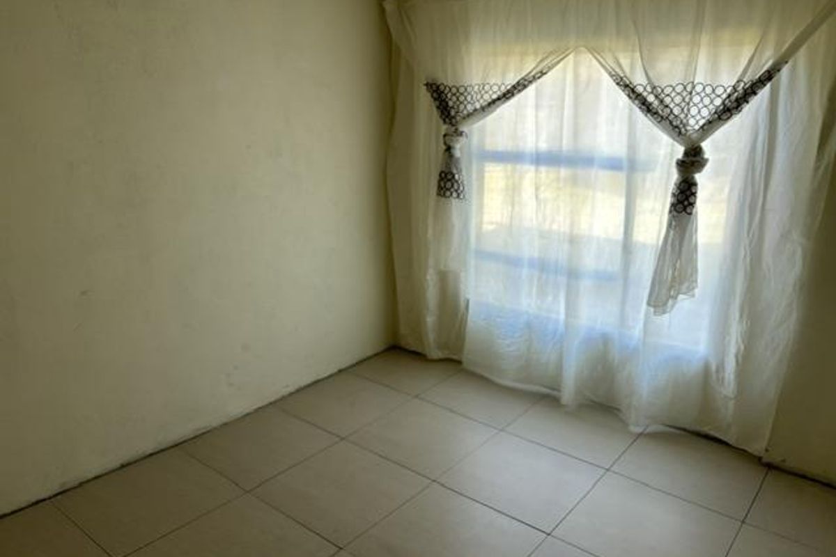 An empty bedroom featuring tiled flooring and a large window, providing a blank canvas for potential interior design updates.