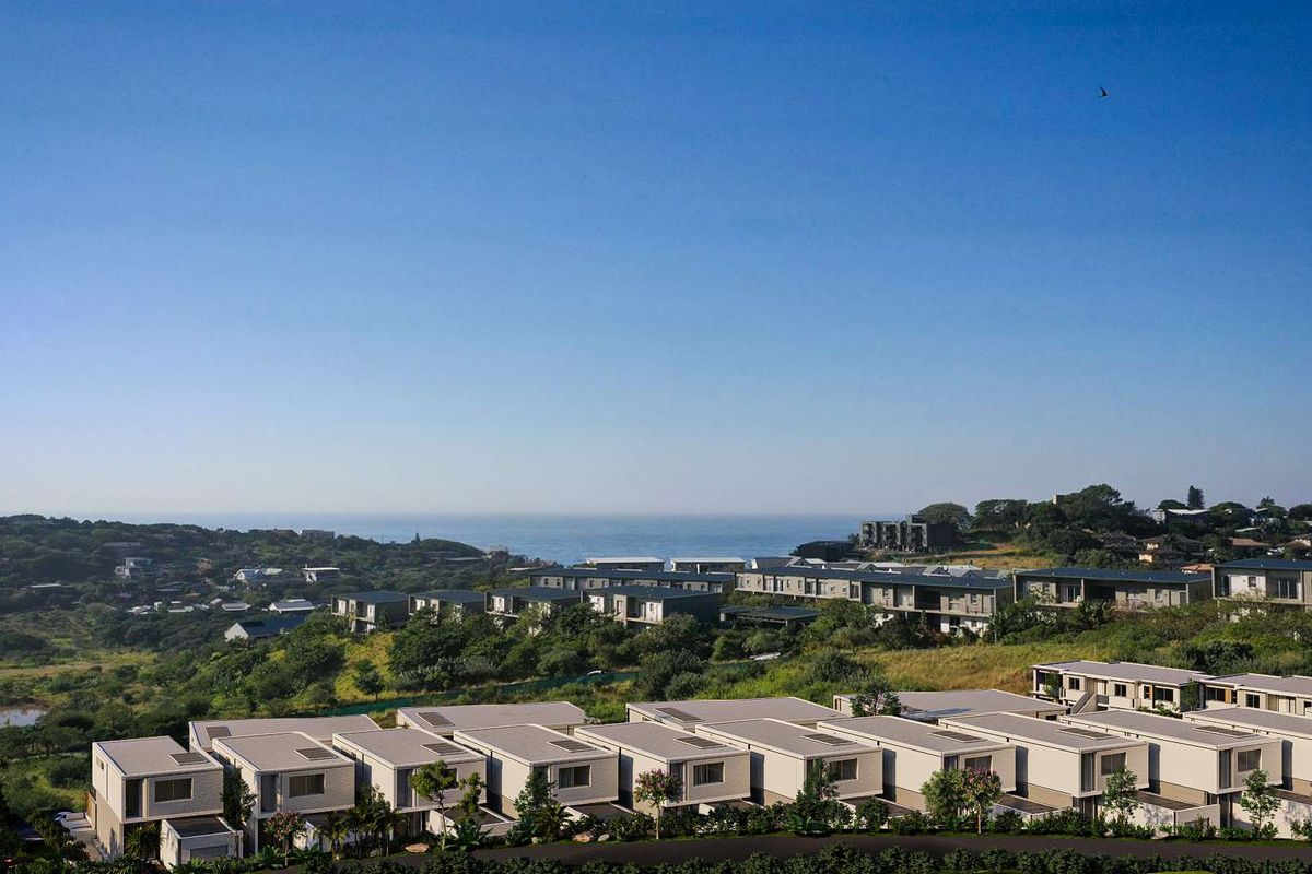 An elevated aerial view of a modern townhouse development situated in a scenic coastal landscape with ocean views.