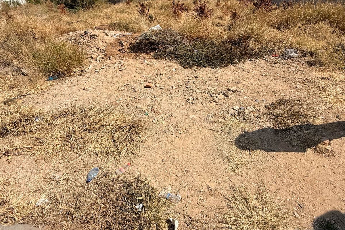 A vacant residential plot featuring dry, overgrown vegetation and a perimeter boundary wall, suitable for future development.