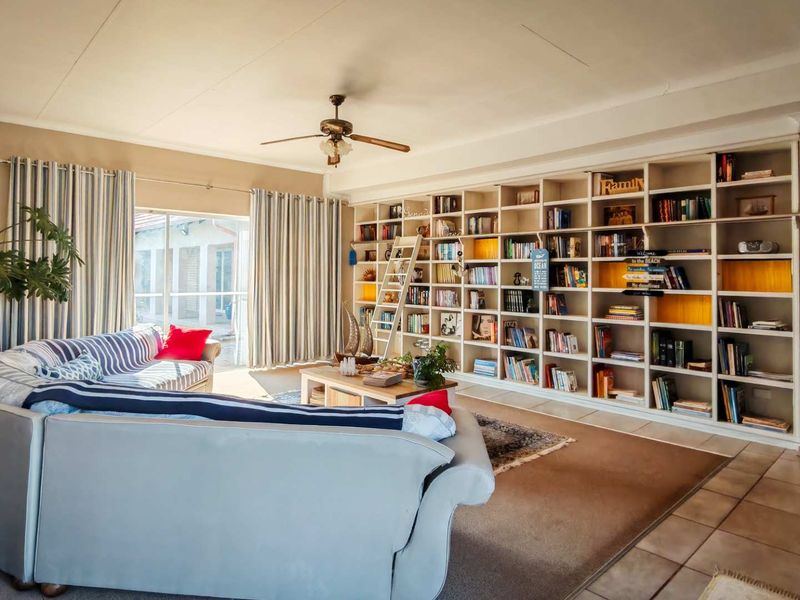 Spacious living room featuring a large built-in floor-to-ceiling bookshelf, ceiling fan, and sliding glass doors providing access to the outdoor area.