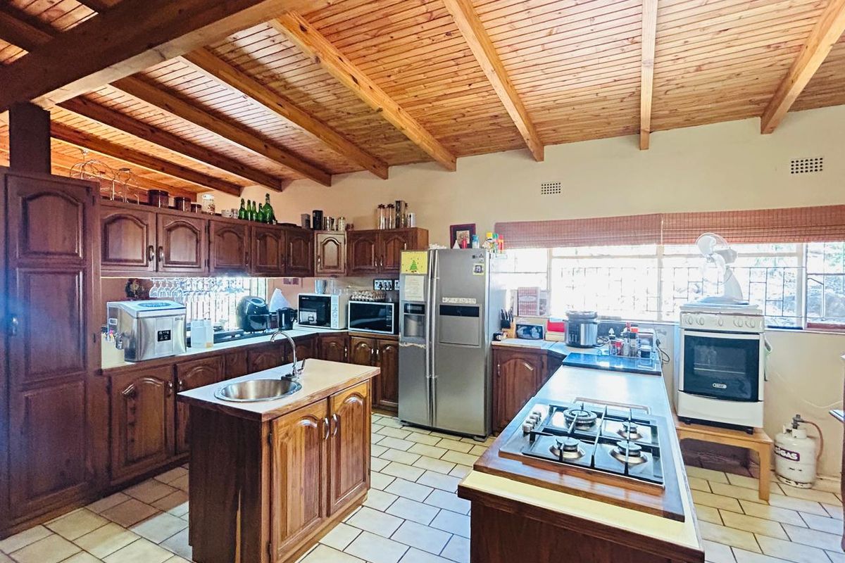 Spacious kitchen featuring timber cabinetry, a central island with sink, built-in gas hob, and exposed timber beam ceiling.