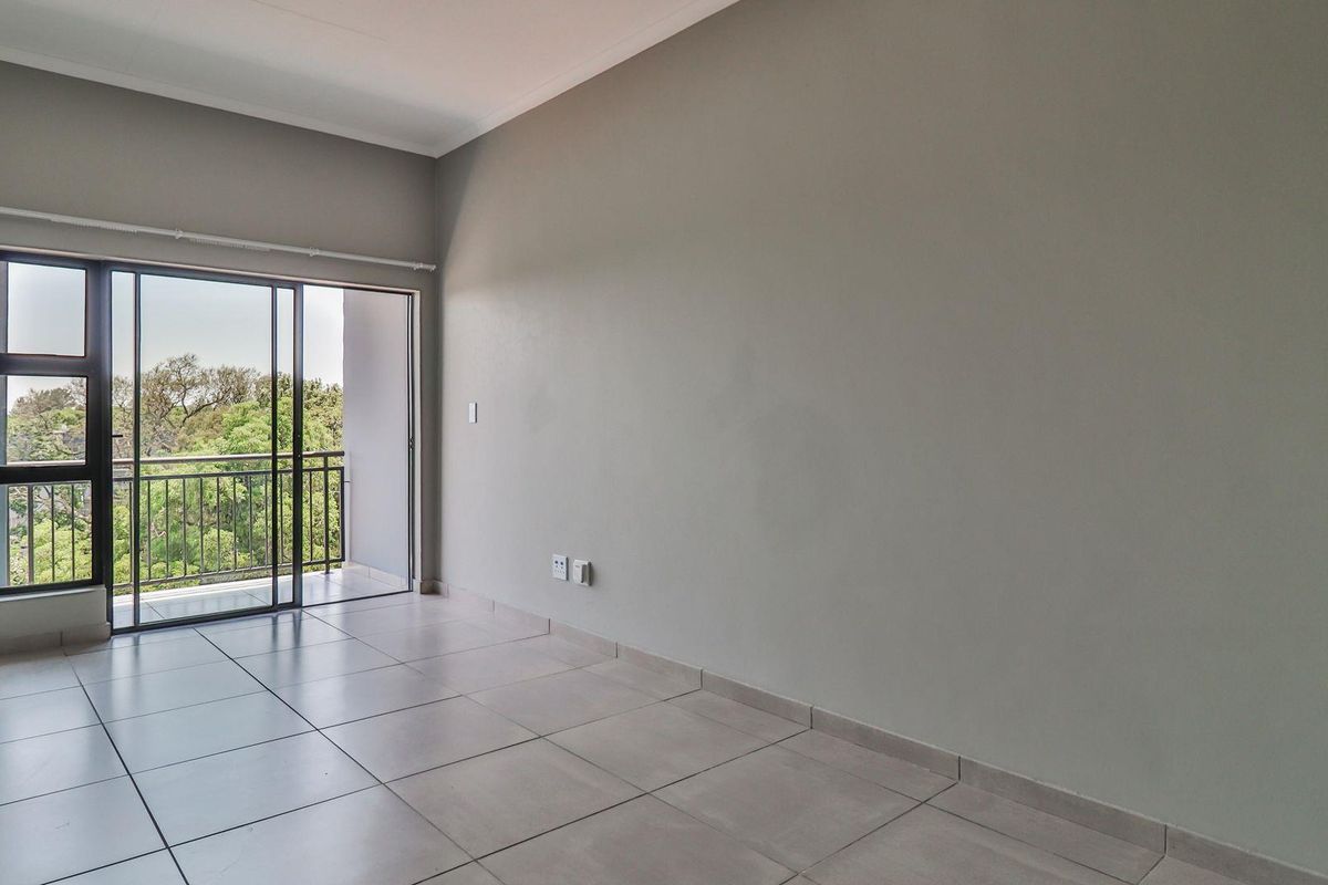 An empty, well-lit living room featuring neutral tiled flooring and a sliding glass door providing access to a private balcony.