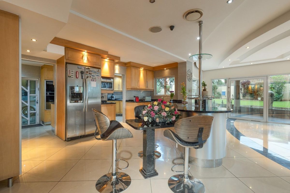 Spacious kitchen featuring light wood cabinetry, granite countertops, a central breakfast bar, and tiled flooring with direct access to the garden.