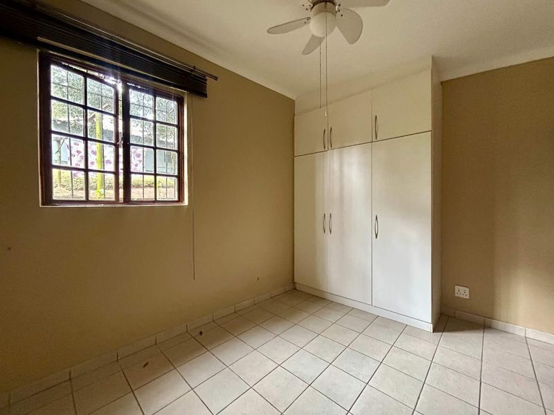 A vacant bedroom featuring tiled flooring, built-in cupboards, and a ceiling fan, offering a blank canvas for personalization.