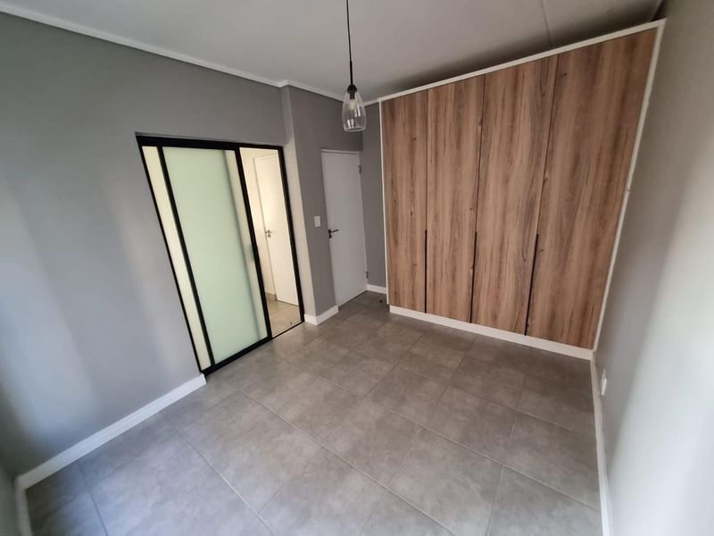 A clean, modern bedroom featuring neutral grey walls, large format floor tiles, and contemporary wood-finish built-in cupboards.