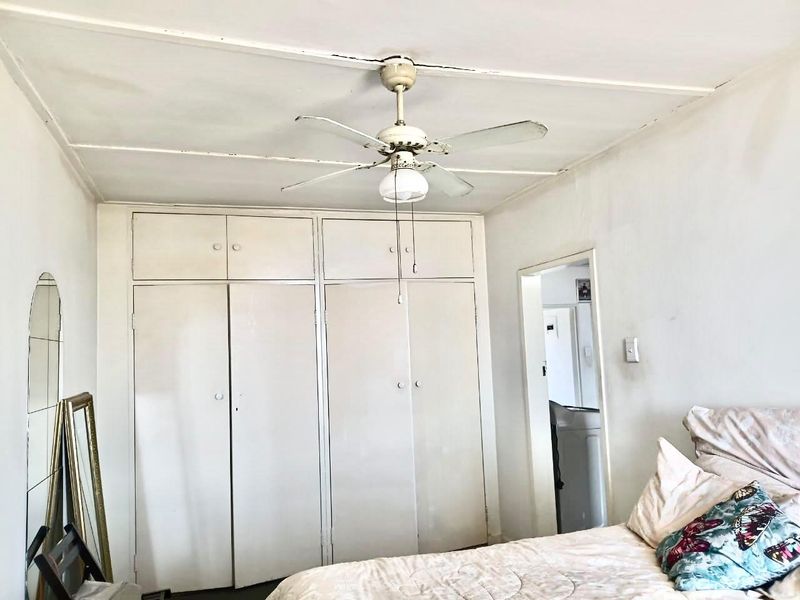 Bedroom featuring built-in cupboards and a ceiling fan, showing signs of wear on the ceiling and cabinetry finishes.