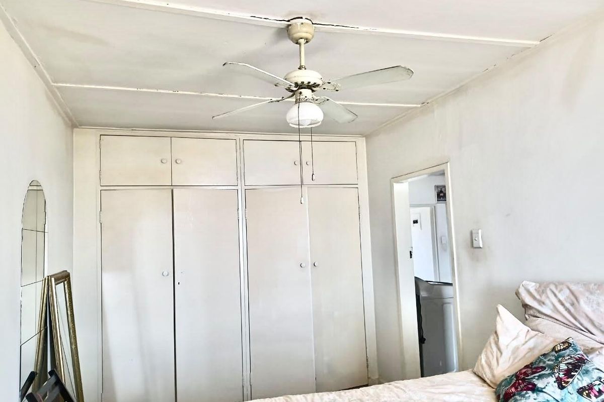 Bedroom featuring built-in cupboards and a ceiling fan, showing signs of wear on the ceiling and cabinetry finishes.