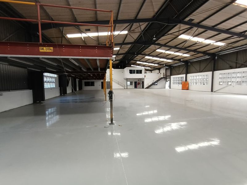 Spacious industrial warehouse featuring a mezzanine level, polished epoxy flooring, high steel truss ceilings with skylights, and ample natural light through glass block windows.