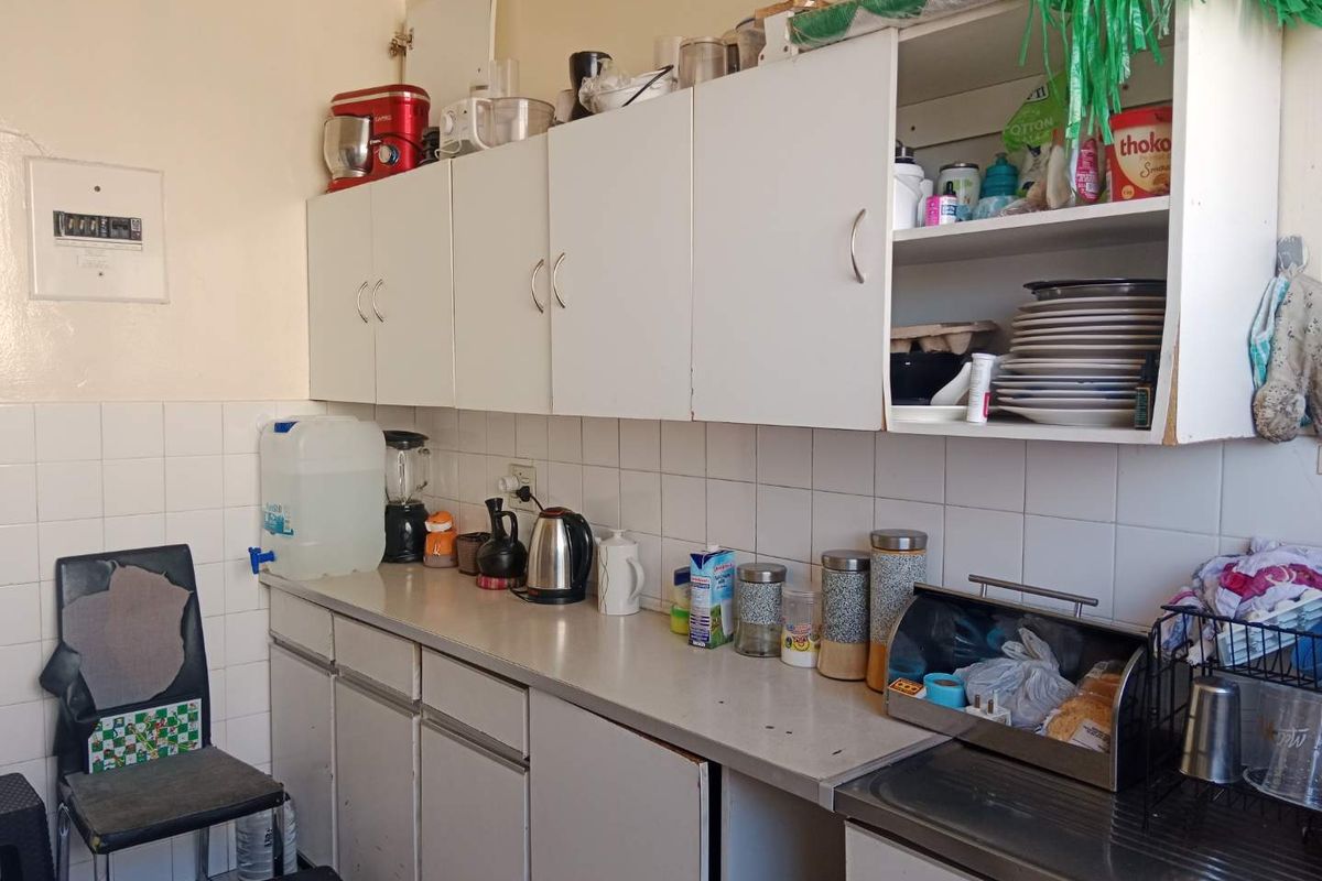 A functional kitchen area featuring white cabinetry, laminate countertops, and a tiled backsplash, offering a practical layout for daily food preparation.