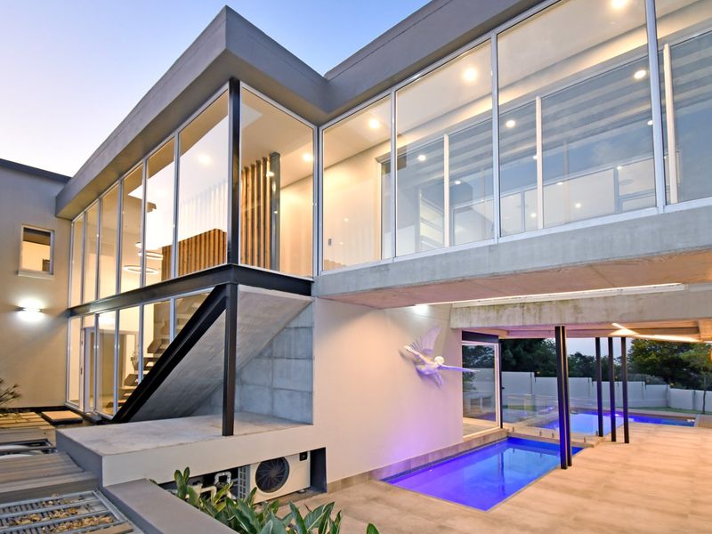 Modern architectural rear elevation featuring extensive floor-to-ceiling glazing, concrete structural elements, and a sleek swimming pool area with integrated lighting.
