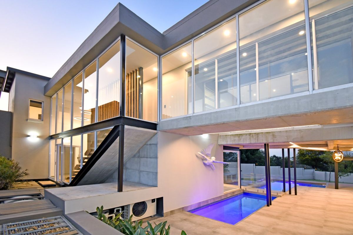 Modern architectural rear elevation featuring extensive floor-to-ceiling glazing, concrete structural elements, and a sleek swimming pool area with integrated lighting.