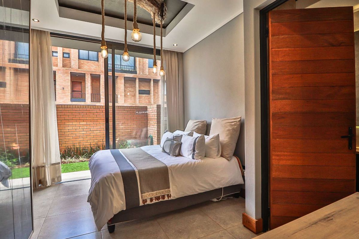 Modern bedroom featuring a tray ceiling, large sliding glass doors opening to a private garden, and warm timber door finishes.