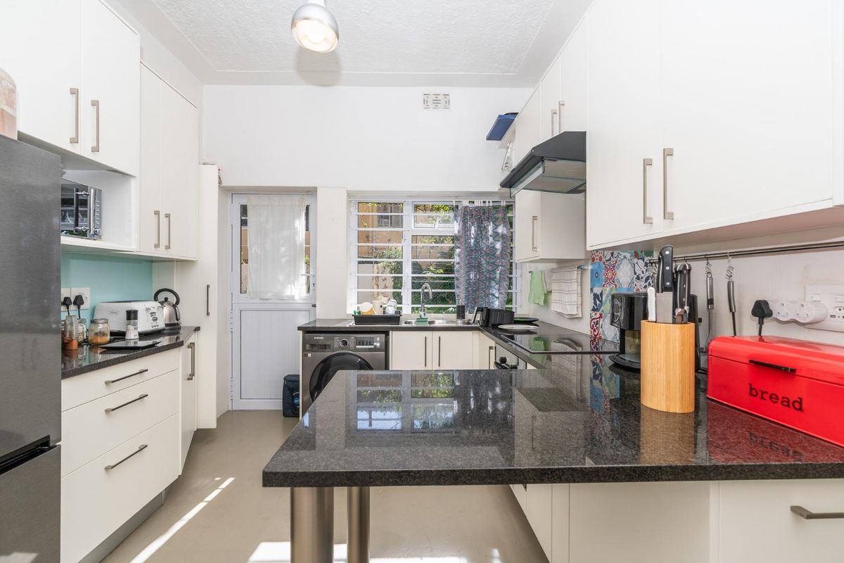 A functional kitchen featuring white cabinetry, dark granite countertops, a built-in extractor fan, and integrated laundry plumbing.