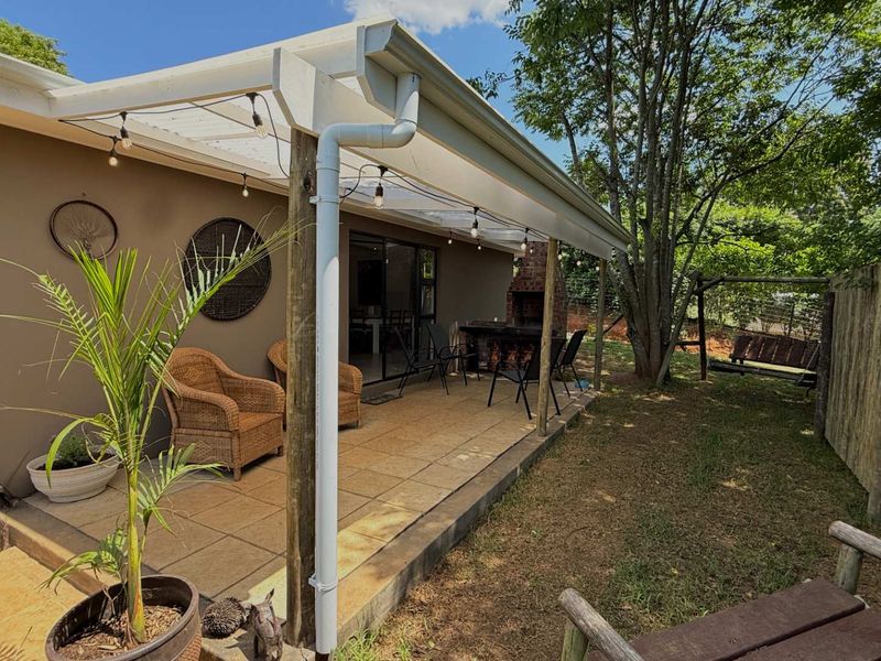 A covered outdoor patio featuring tiled flooring, timber support posts, and a built-in brick braai, perfect for outdoor entertaining.