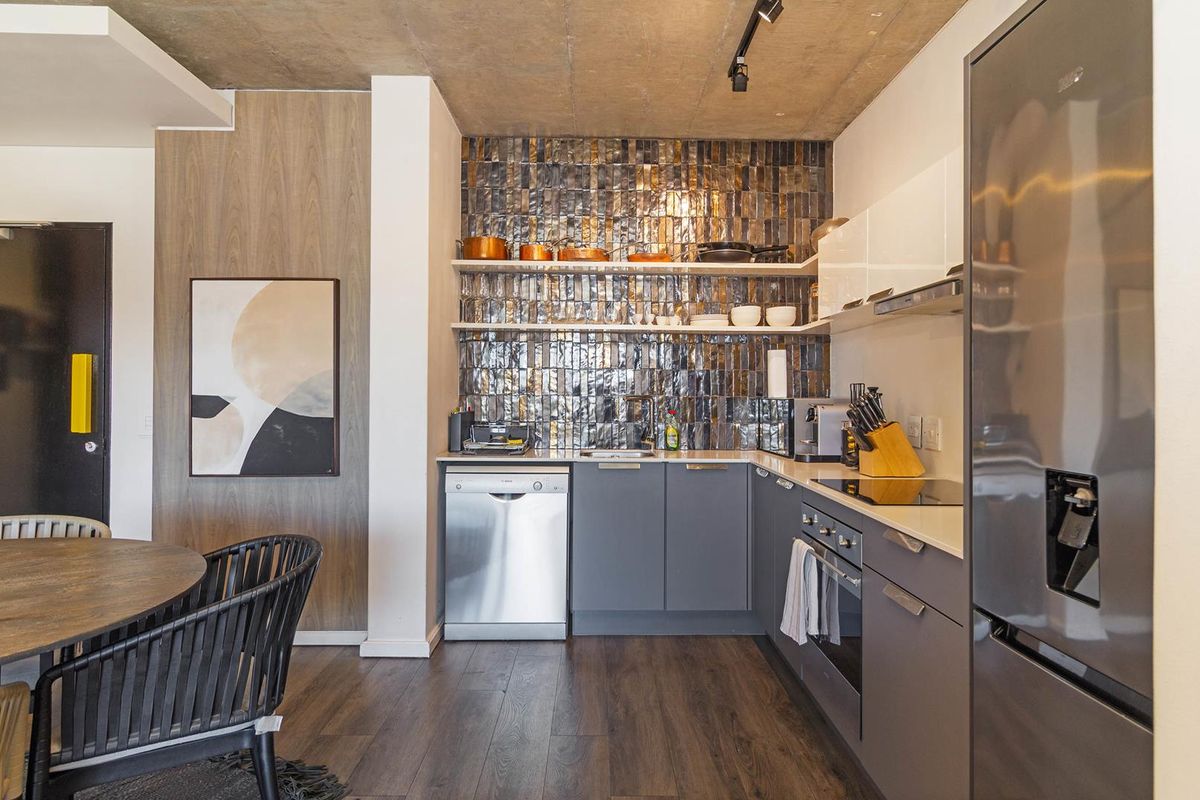 Modern kitchen featuring sleek grey cabinetry, integrated appliances, a striking metallic tiled backsplash, and an exposed concrete ceiling.