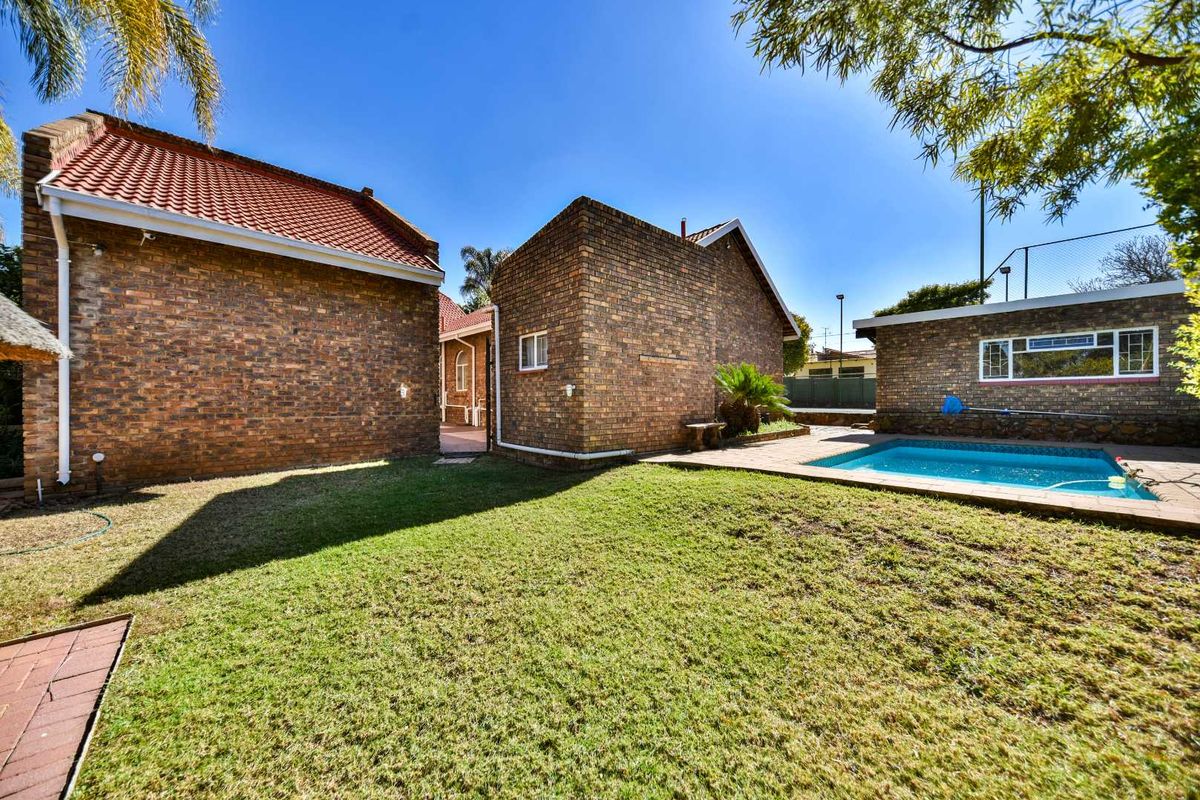 Rear exterior view featuring a brick house, a swimming pool with paved surround, and a well-maintained lawn area.