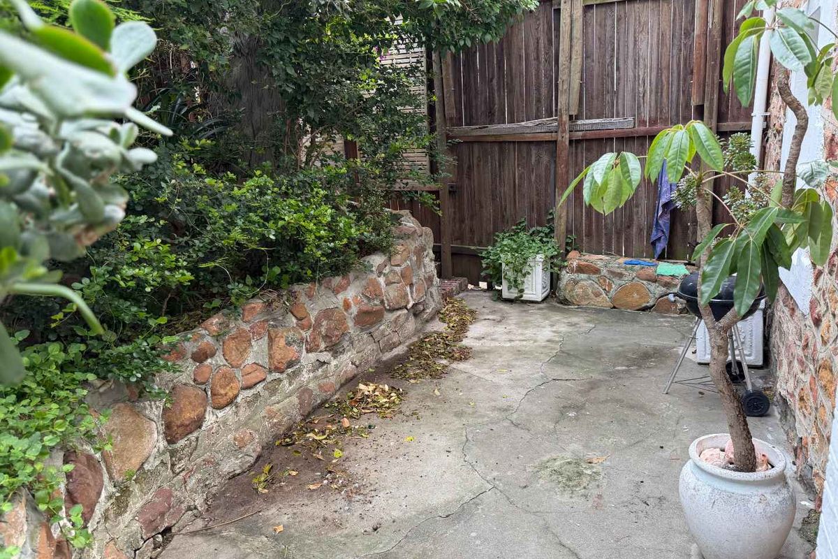 A private rear courtyard area featuring a stone retaining wall, concrete paving, and timber boundary fencing, offering potential for landscaping and outdoor improvement.