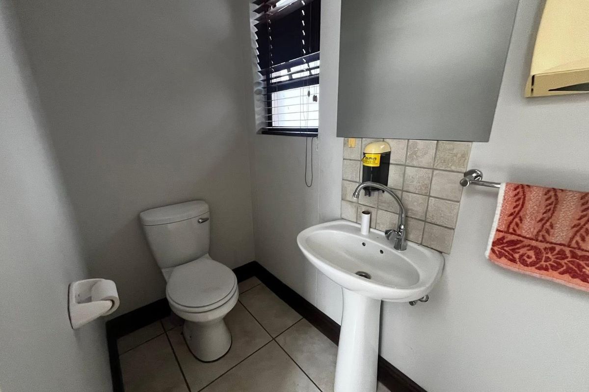 A functional guest bathroom featuring a pedestal basin, tiled splashback, and standard toilet with tiled flooring and window blinds.