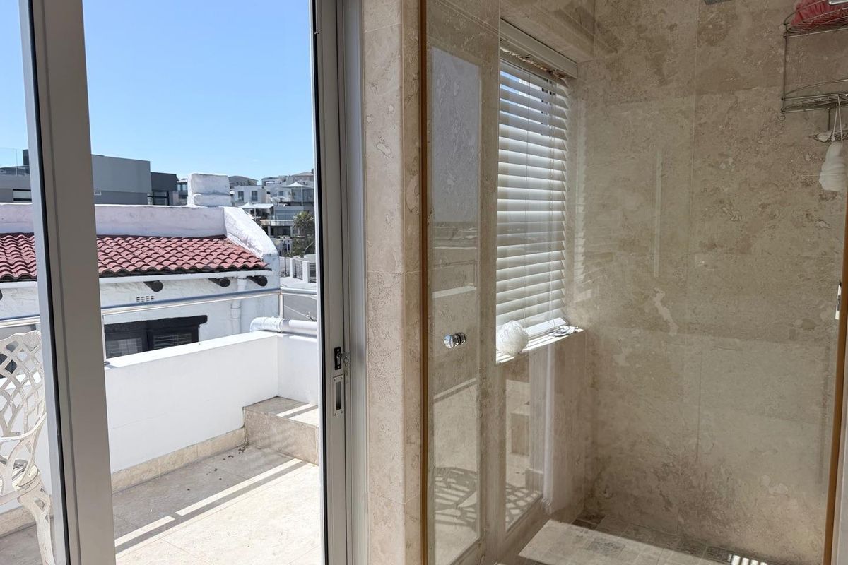Modern bathroom featuring stone wall tiling, a glass-enclosed shower with a rain shower head, and direct access to an outdoor balcony.