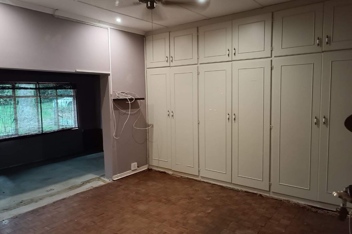A bedroom featuring extensive built-in floor-to-ceiling cabinetry, parquet flooring, and a ceiling fan, with an adjacent room visible through a wide opening.