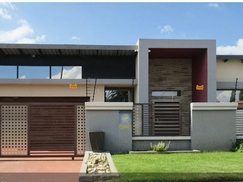 Modern front elevation featuring a contemporary facade, stone cladding accents, secure sliding gate, electric fencing, and a well-maintained front lawn.