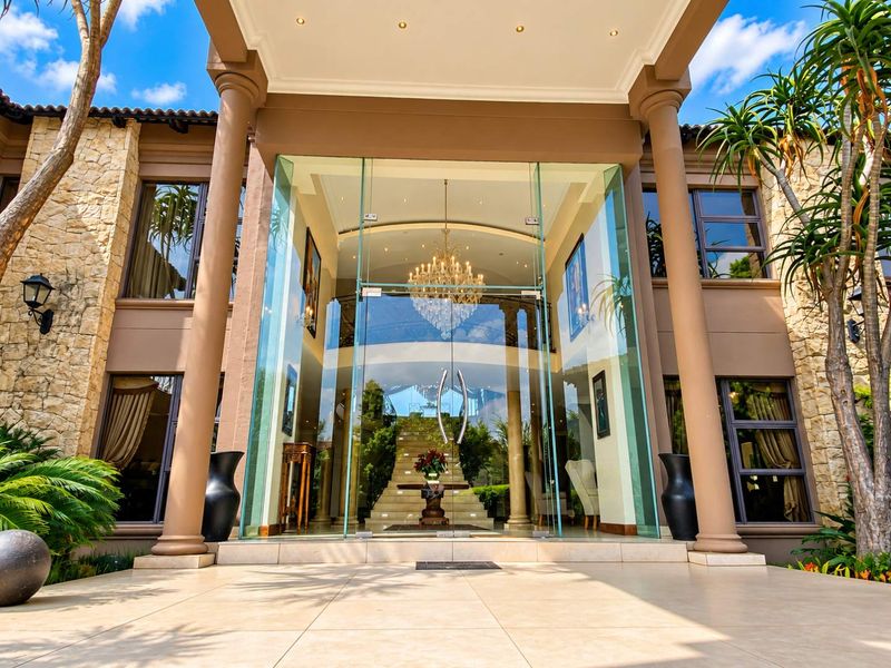 Grand front entrance featuring a double-volume glass facade, stone cladding, and a prominent staircase visible through the main door.
