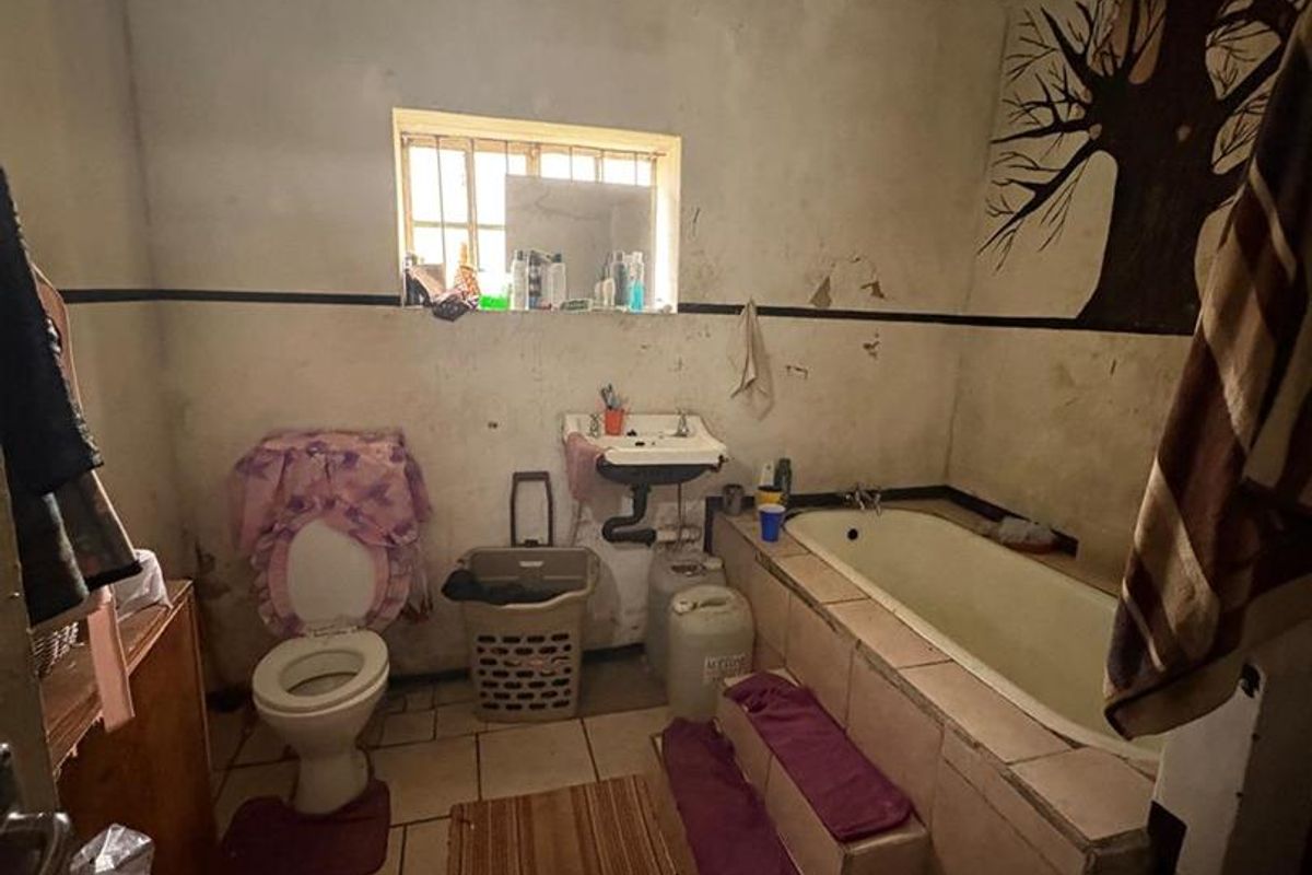 A dated bathroom featuring a built-in bathtub with tiled steps, a standard toilet, and a wall-mounted basin, requiring significant cosmetic renovation and repair.