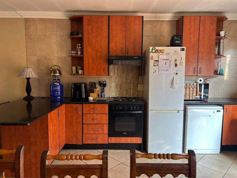 Functional kitchen featuring warm-toned wooden cabinetry, granite countertops, built-in oven and hob, and tiled finishes throughout.